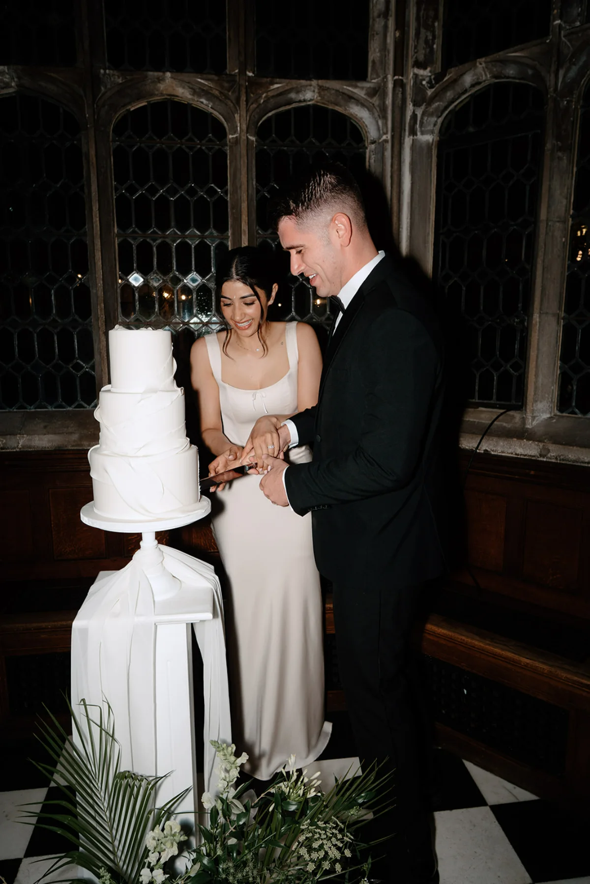 A bride and groom cut their three-tiered white wedding cake at their reception.