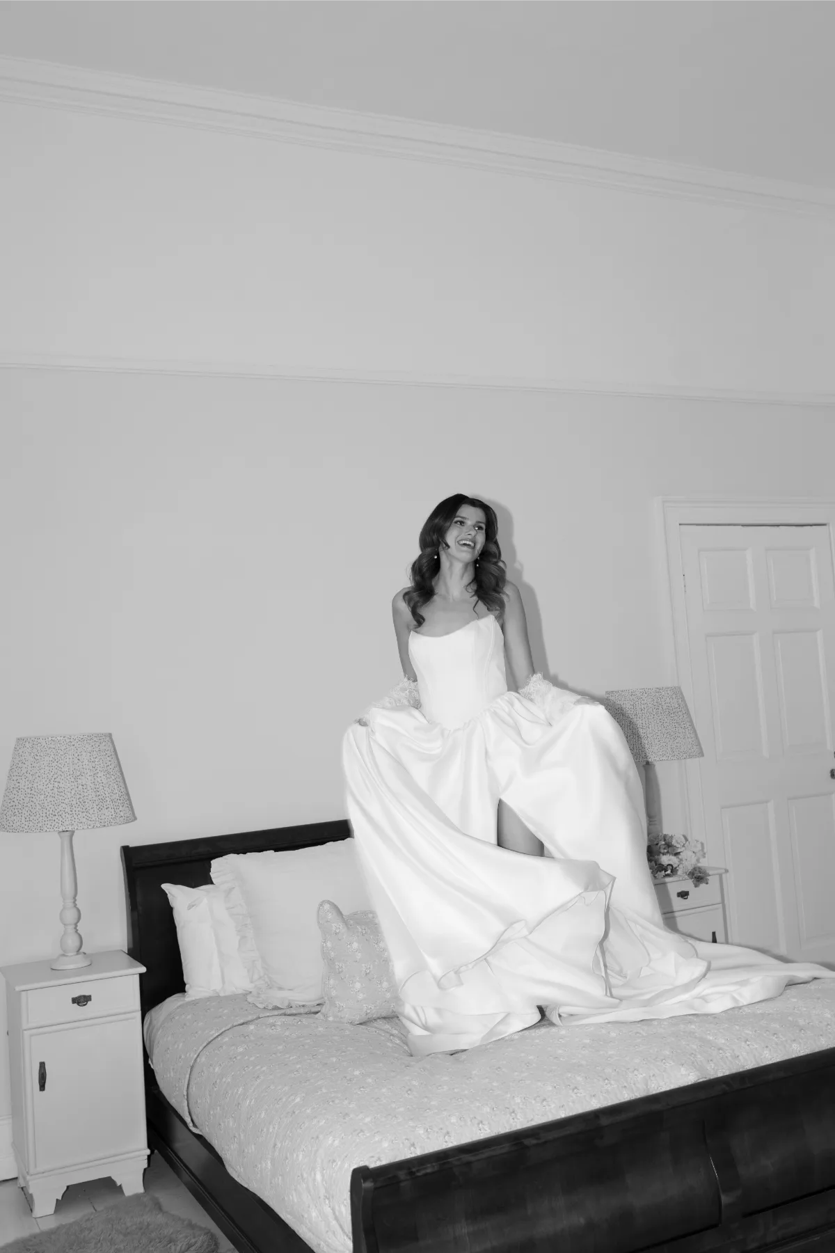 A bride poses in a wedding dress while jumping on a bed, wearing makeup by Suffolk bridal makeup artist Emily Chantal.