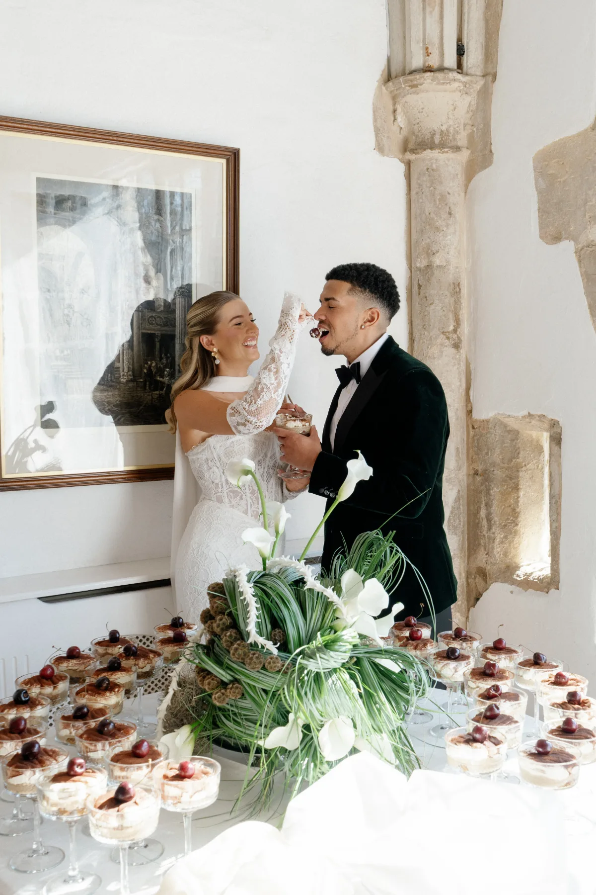 A bride feedsa cherry to her husband in front of a table of desserts, wearing makeup by Suffolk makeup artist Emily Chantal.