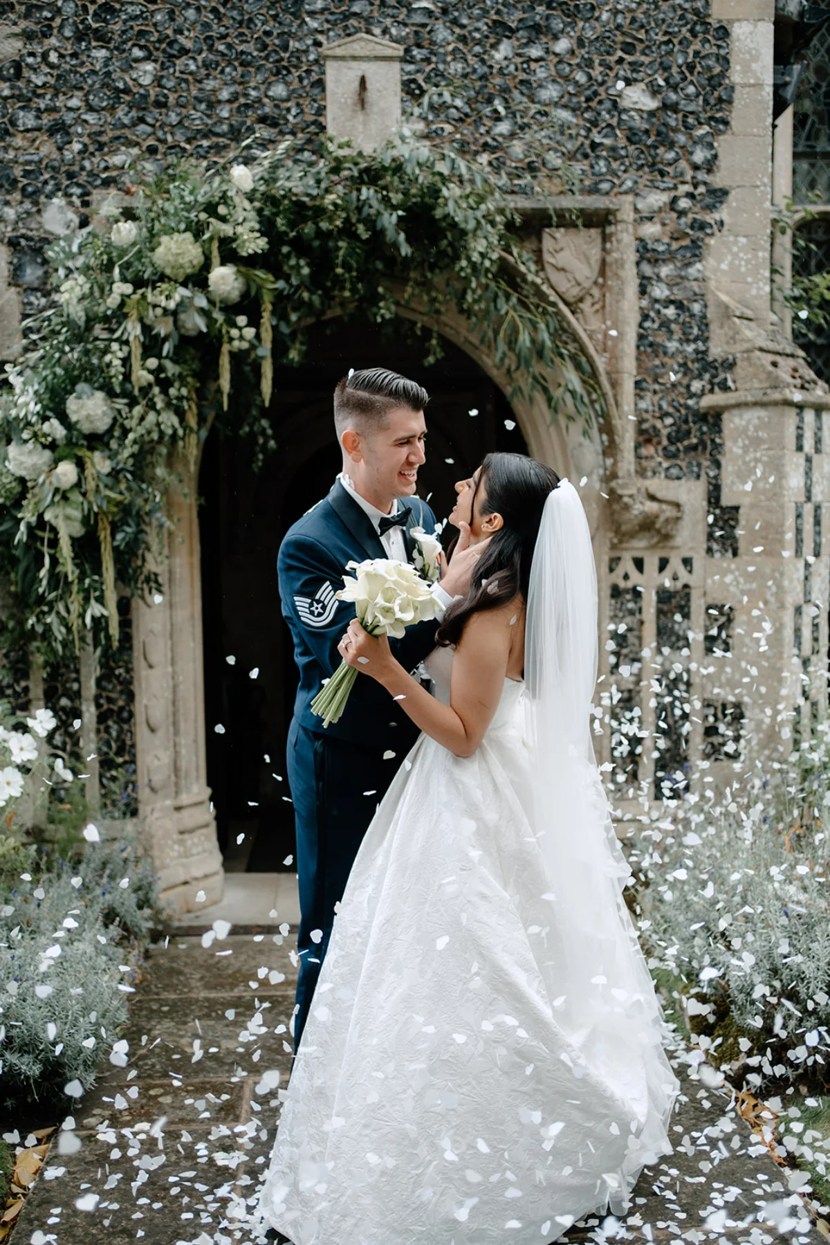 A bride and groom smile at each other, surrounded by falling confetti, at Hengrave Hall in Suffolk.