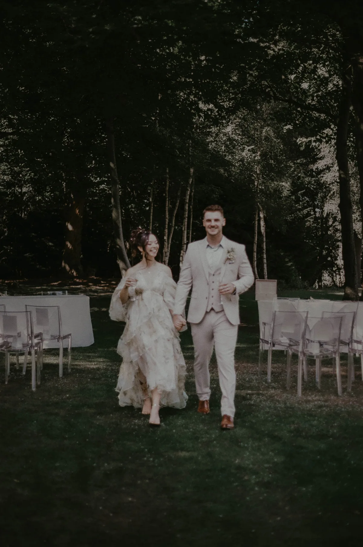 A bride and groom walk back down the aisle with Champagne glasses in hand, and confetti on the floor. 35mm film wedding photography in Suffolk by Mikaela Jade.