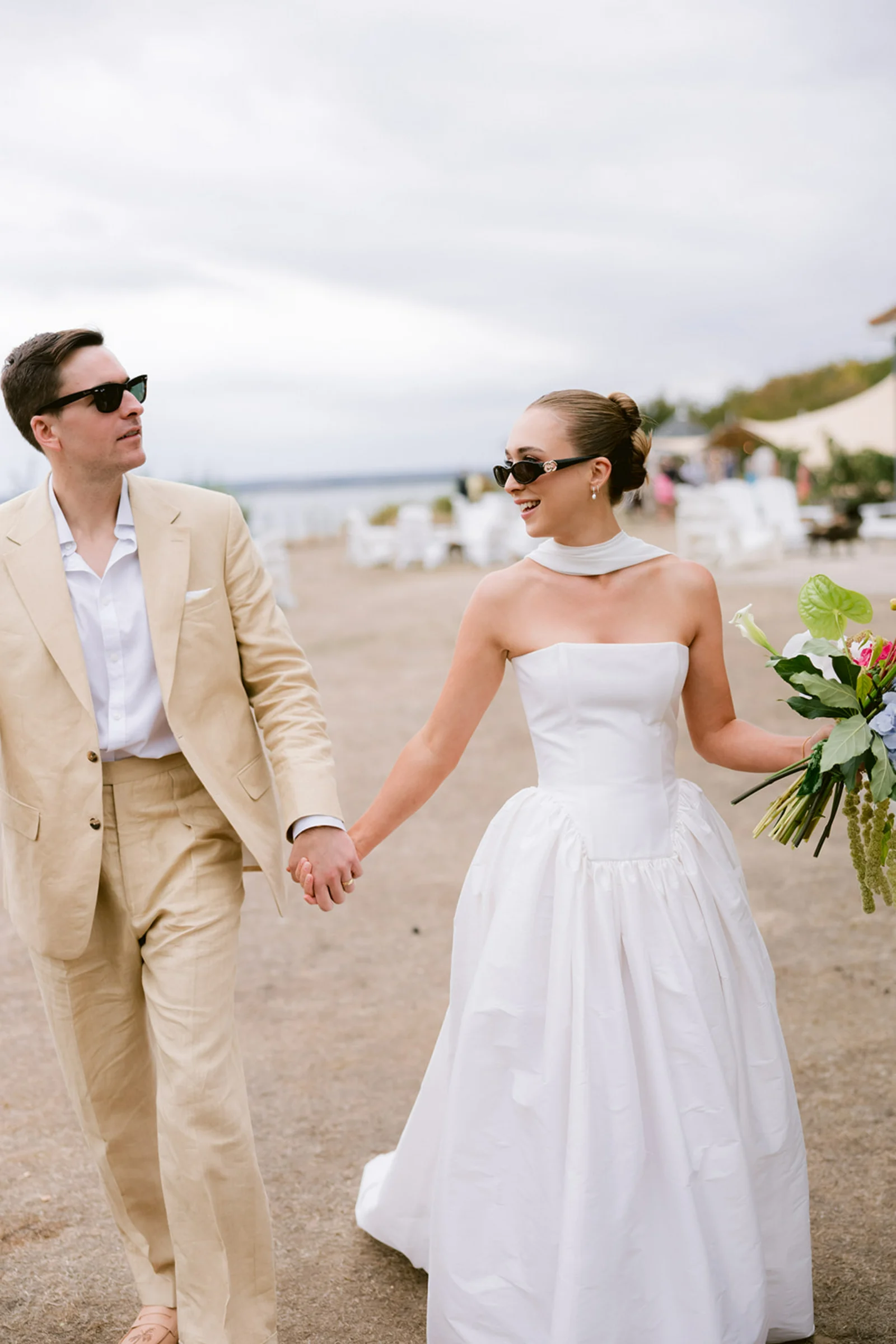 Bride and groom wearing sunglasses walk hand-in-hand on Osea Island.