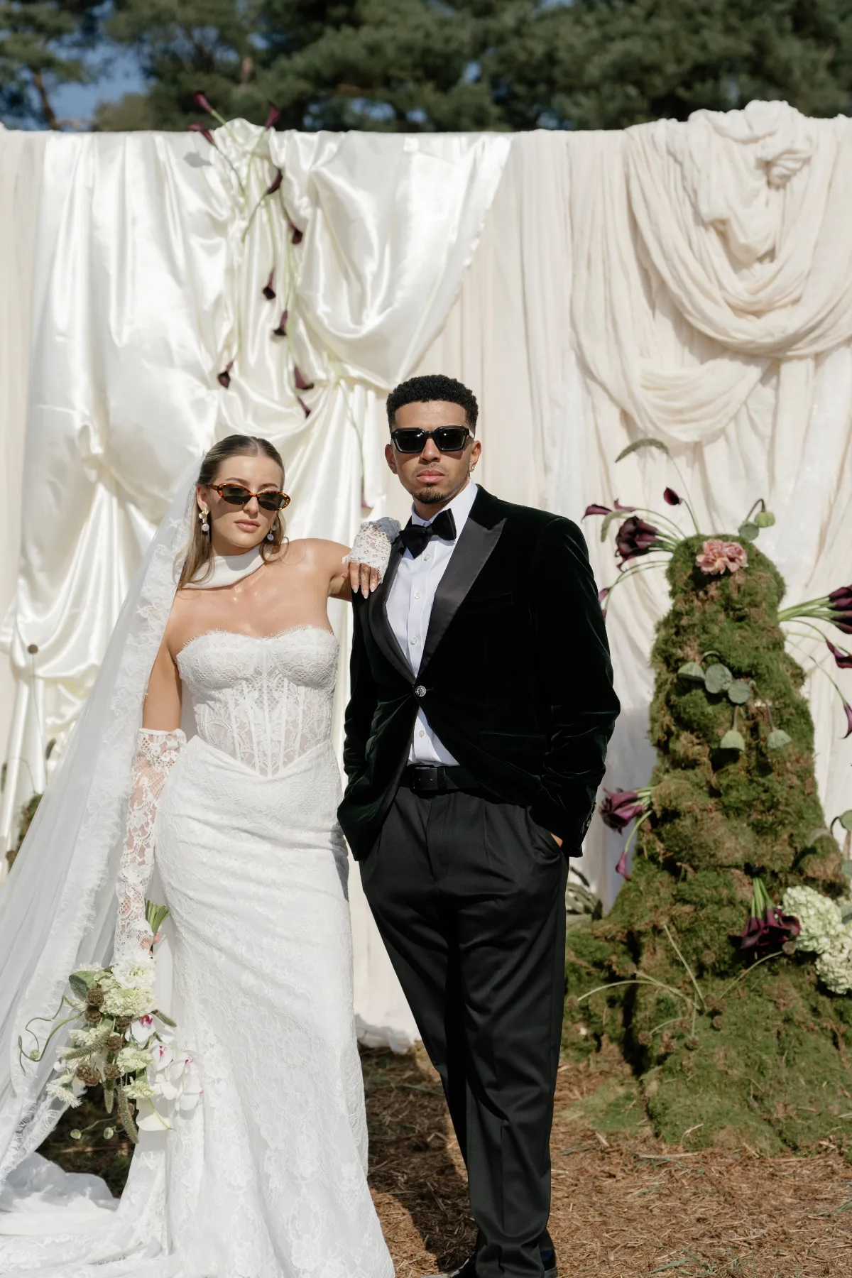 A bride and husband wear sunglasses while looking coolly at the camera, wearing makeup by Suffolk makeup artist Emily Chantal.