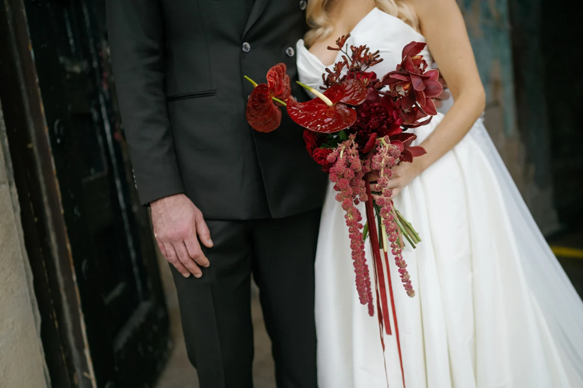 Close up of a bride and groom on their wedding day - the bride holds a bouquet of deep burgundy flowers