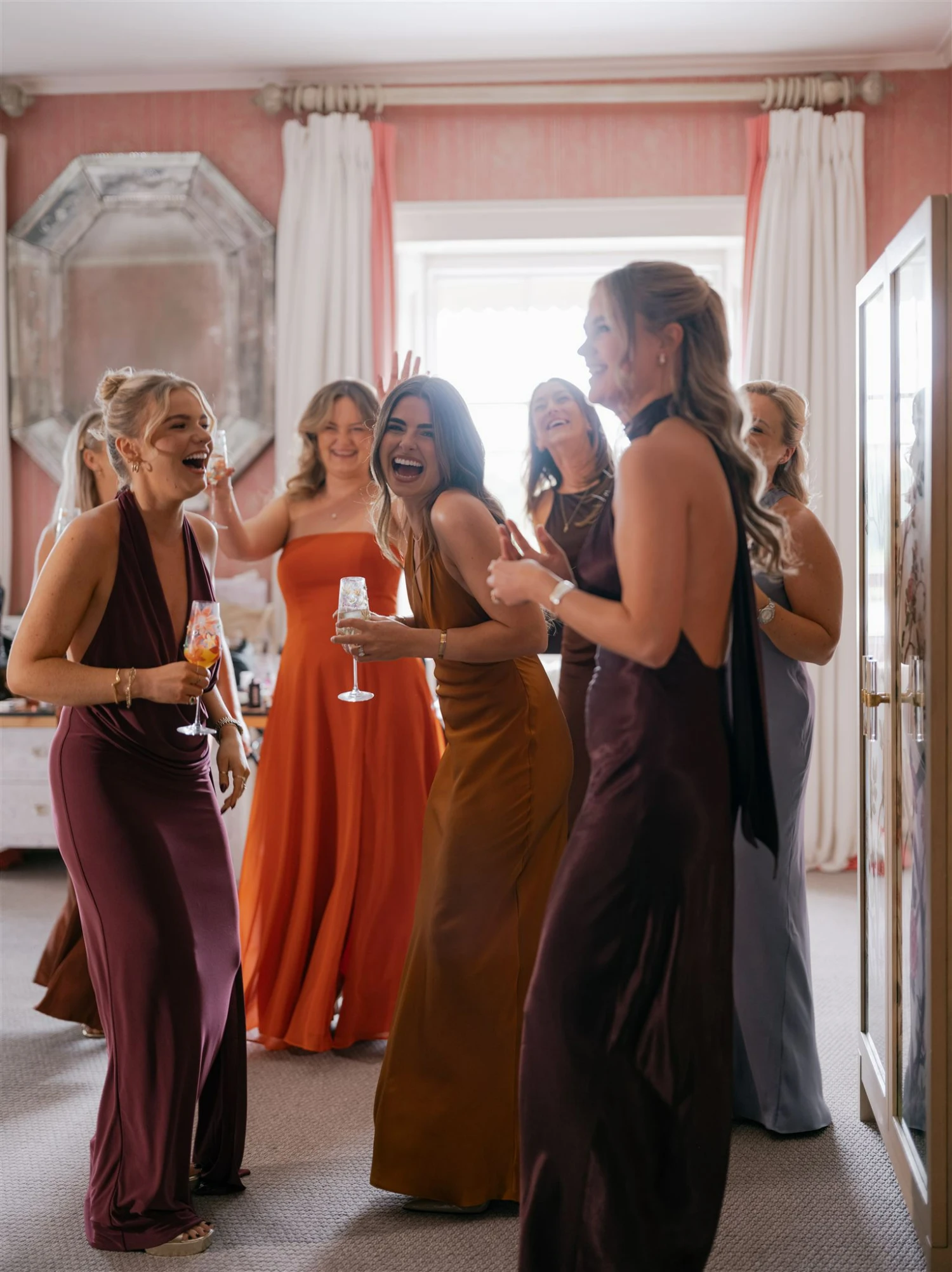 Bridesmaids dancing and smiling before the ceremony, Champagne glasses in hand.