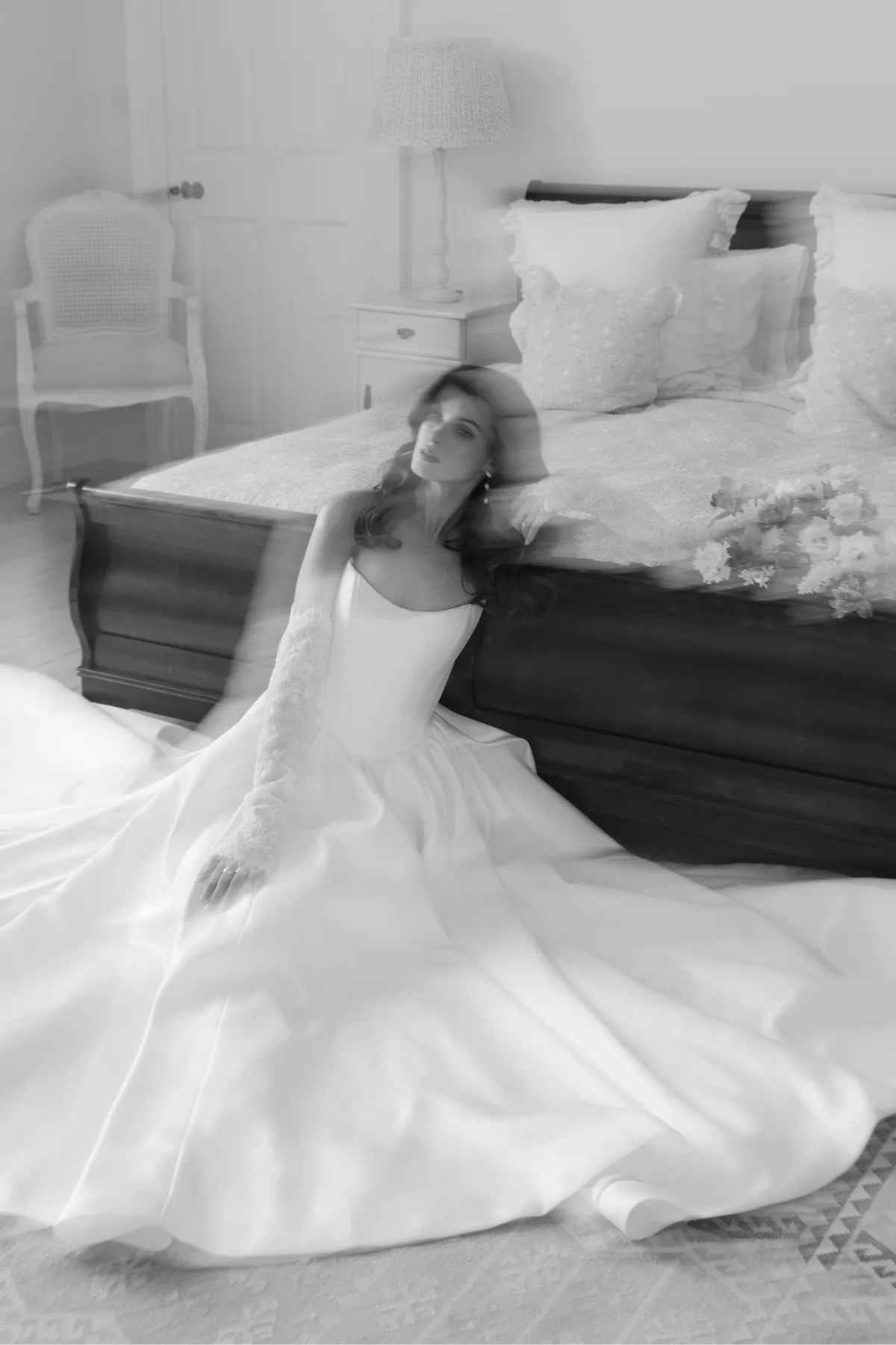 A bride poses in a wedding dress by a bed, wearing makeup by Suffolk bridal makeup artist Emily Chantal.