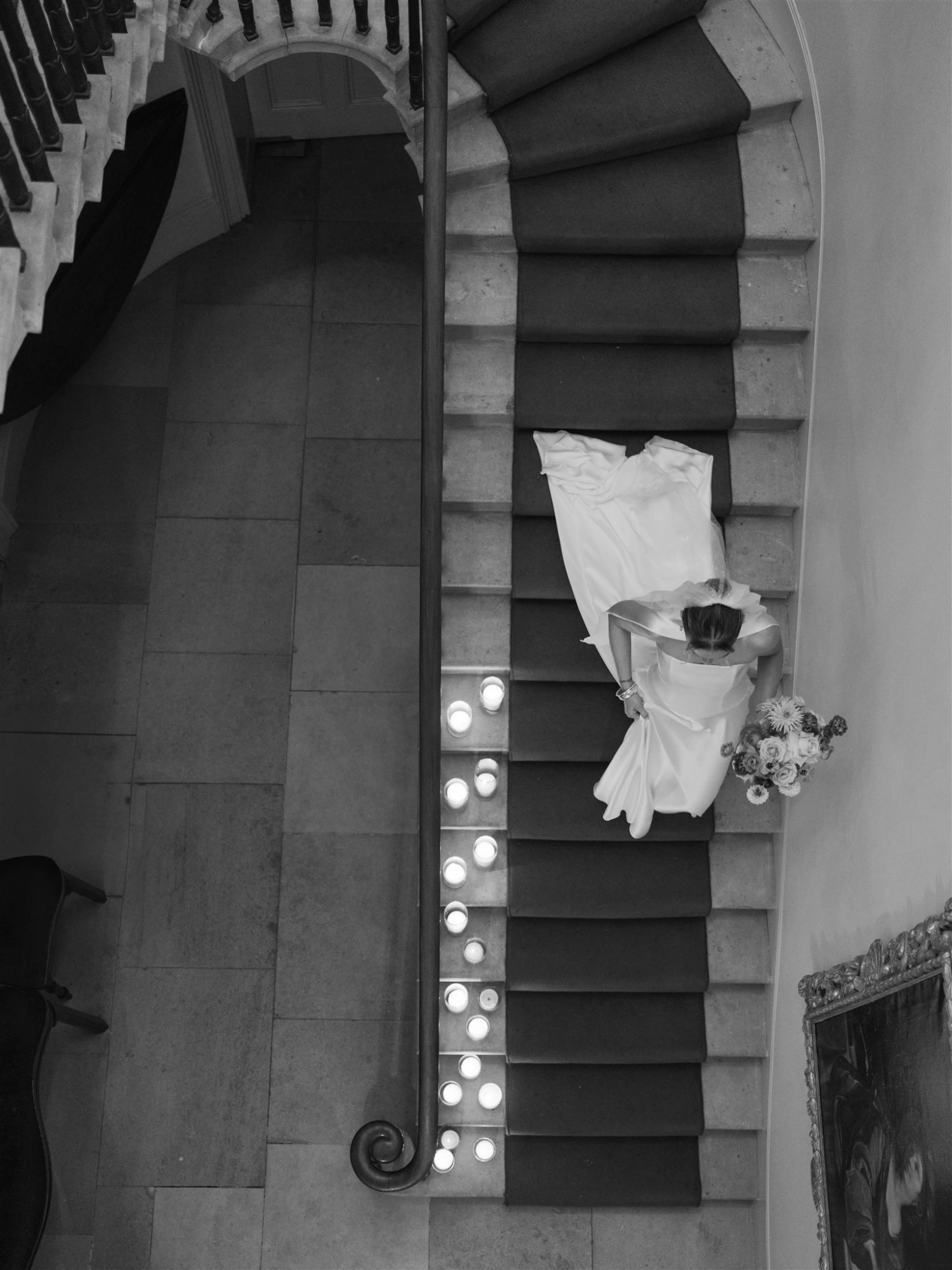 A bride makes her way down a grand staircase with her boquet in hand. Birdseye view.
