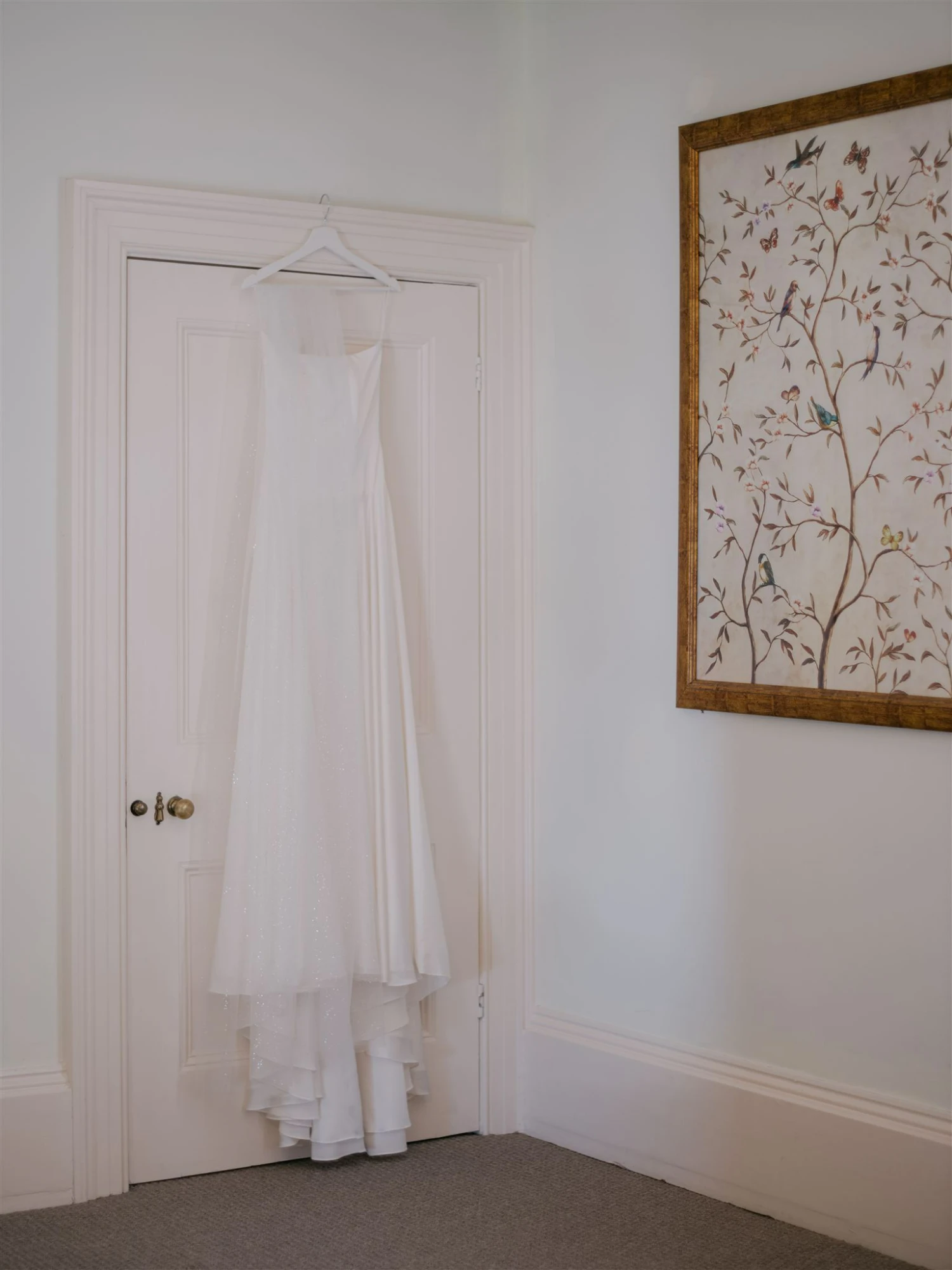 A bride facing a window wearing a long wedding dress and veil - there is a soft glow to the image.