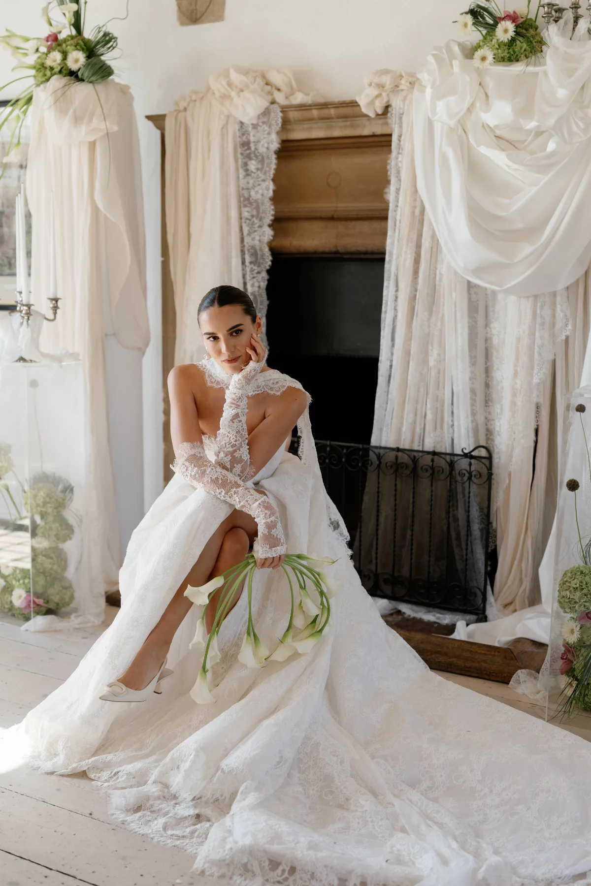 A bride wearing a wedding dress poses in front of an unlit fireplace while seated, wearing makeup by Suffolk makeup artist Emily Chantal.
