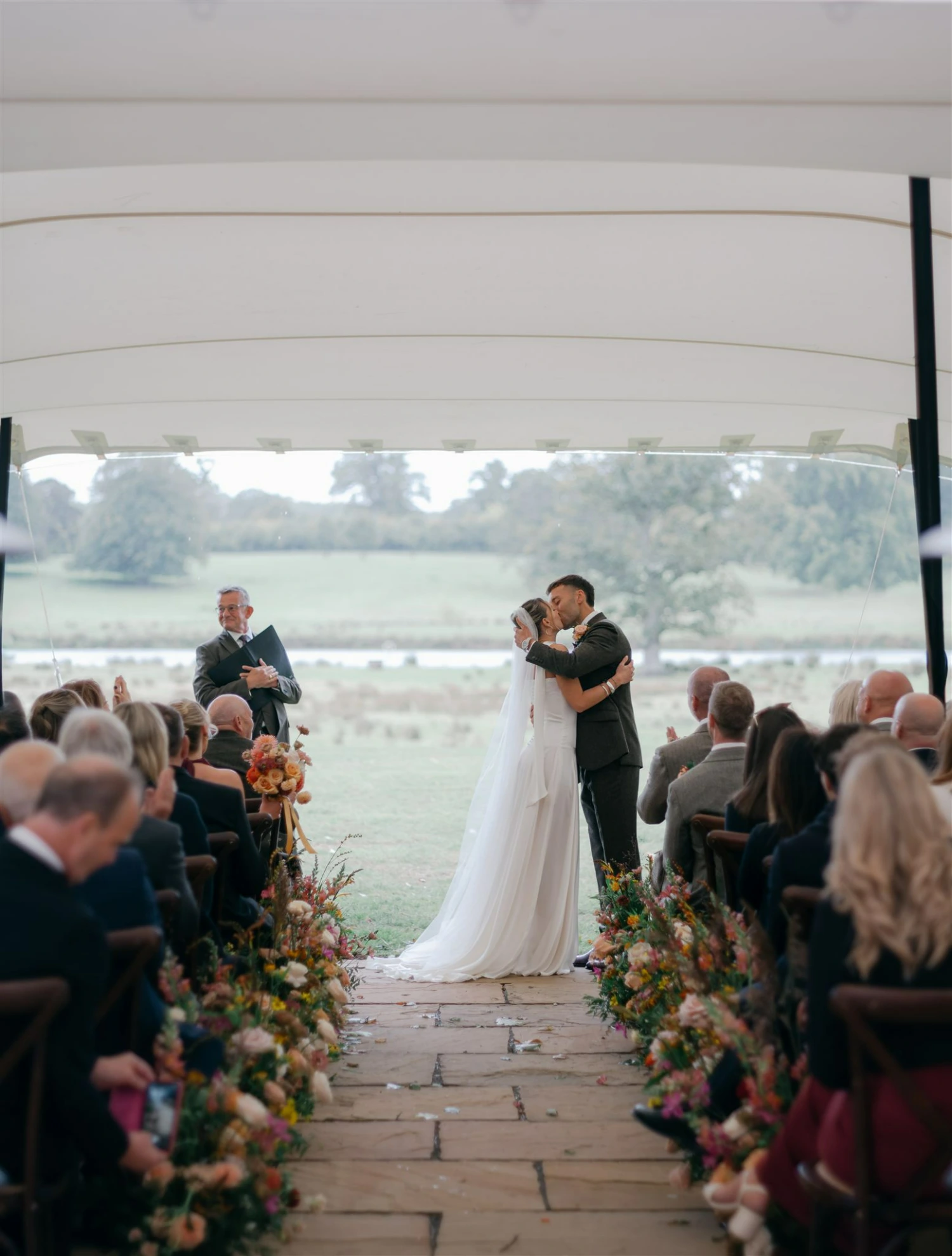A couple kiss at the end of the wedding ceremony, surrounded by seated wedding guests.