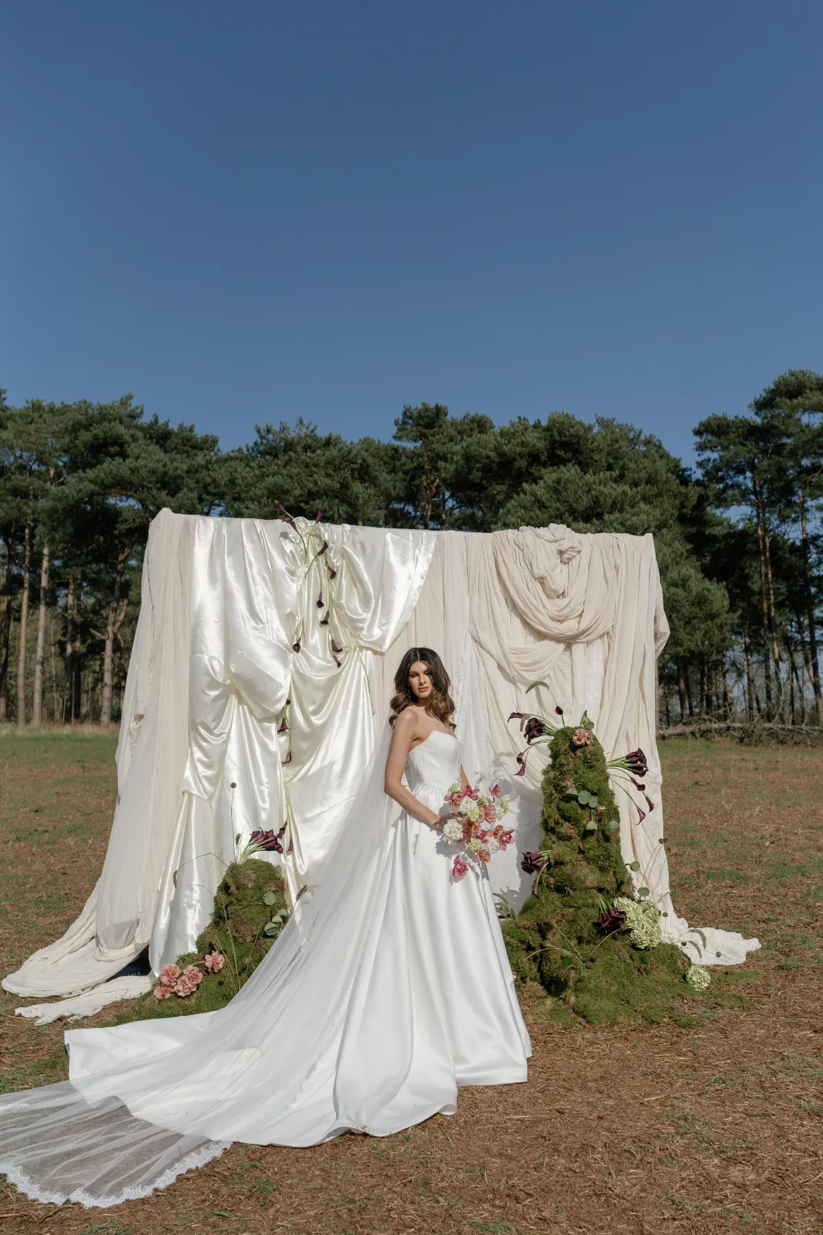 A bride poses in a wedding dress in front of a backdrop of white fabric, wearing makeup by Suffolk bridal makeup artist Emily Chantal.