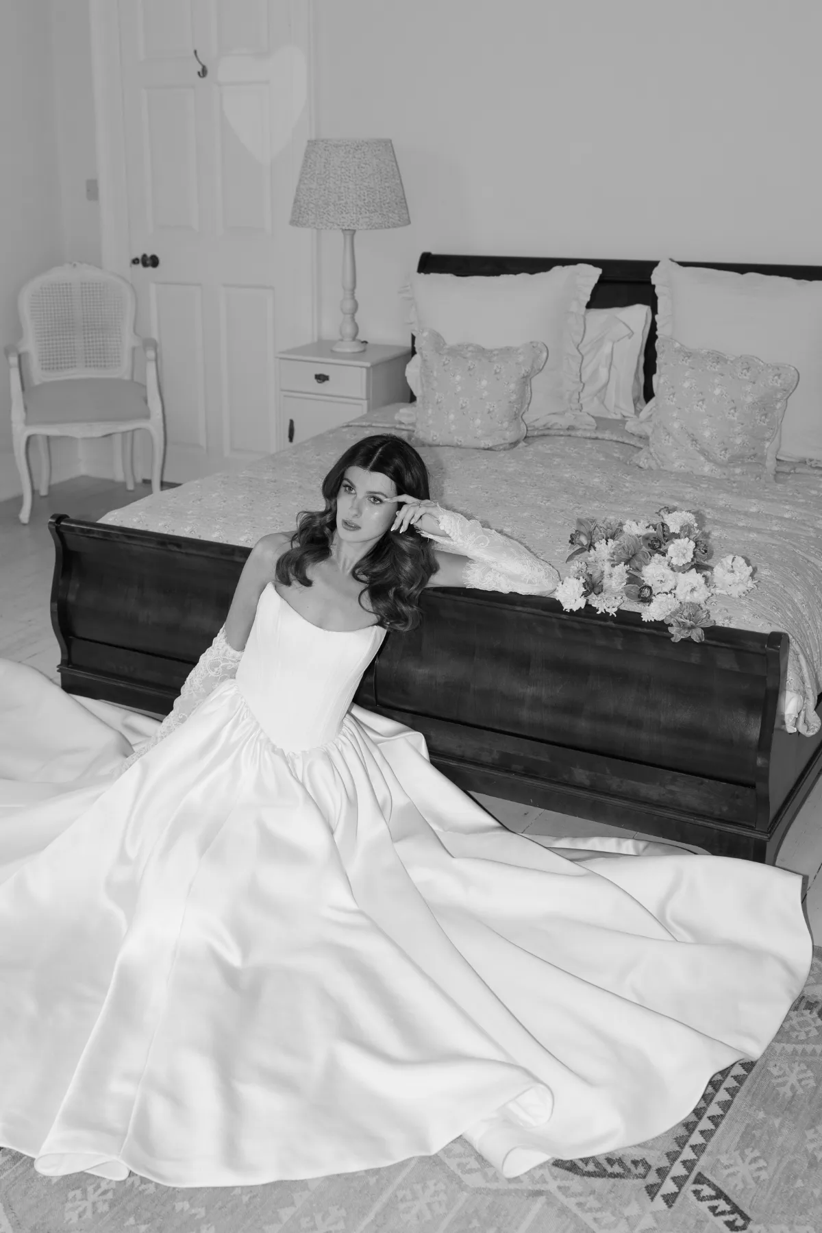 A bride poses in a wedding dress by a bed, wearing makeup by Suffolk bridal makeup artist Emily Chantal.
