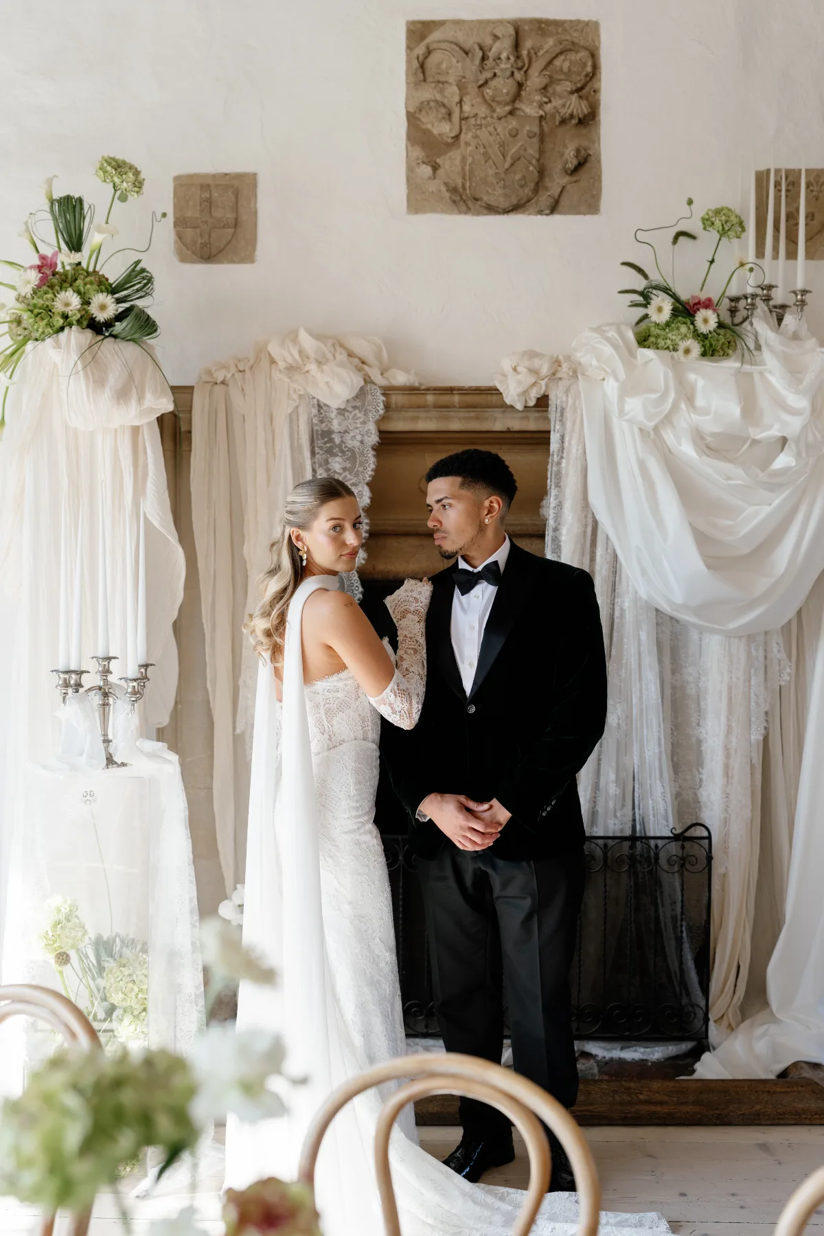 A bride looks over her shoulder at the camera while posing with her husband, wearing makeup by Suffolk makeup artist Emily Chantal.