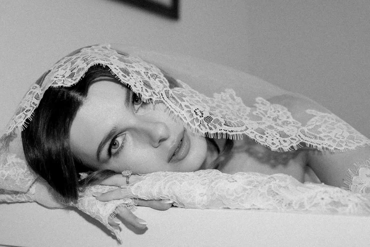 A bride poses in a lace veil and rests her head on her hands, wearing makeup by Suffolk bridal makeup artist Emily Chantal.