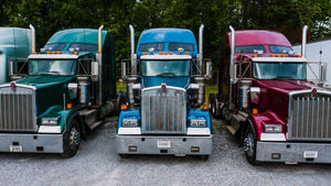 Green, blue, and burgundy semi trucks parked side by side.