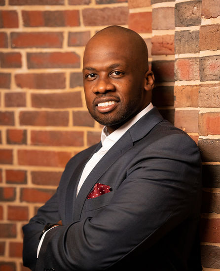 Bald man wearing gray suit jacket and posed sideways, smiling at camera.