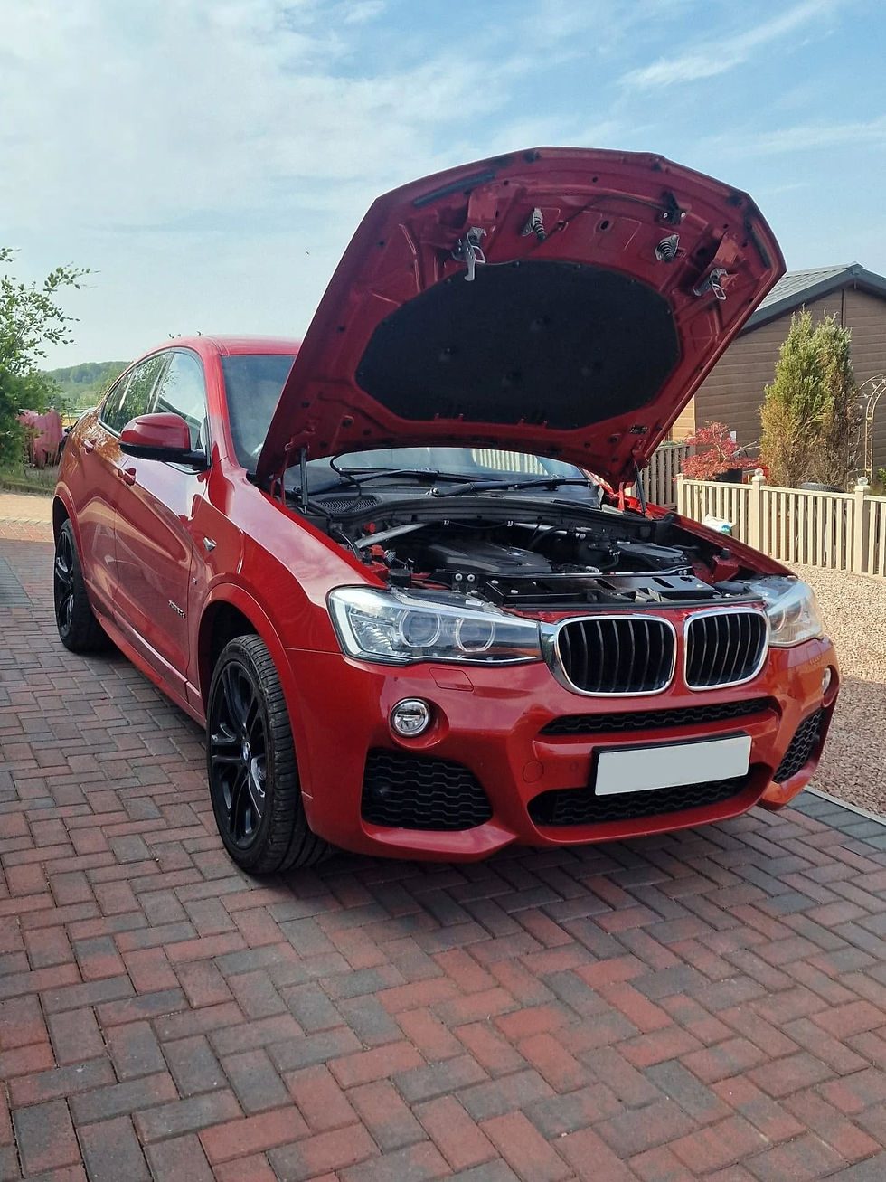 Red BMW SUV parked on a paved driveway with its hood open for maintenance or inspection.