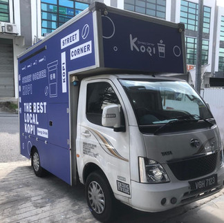 Sticker lorry with a bold blue design displaying a tech service brand and clear contact details, parked in a business area.