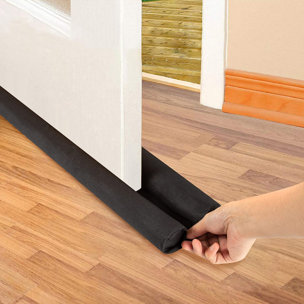 Hand adjusts a black door draft stopper under a white door on a wooden floor. Light from outside suggests a bright day.