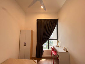 Bilik tidur kecil dengan dinding berwarna krim, almari putih, katil bujang, kerusi merah, dan meja di tepi tingkap. Cahaya matahari menembusi langsir coklat.