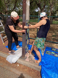 Two women installing a mosaic on a stobie pole