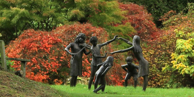 Statues of children playing with autumn shrubs and trees behind.