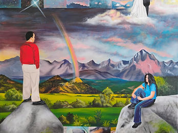 Person standing on a rock looking over a colorful valley with mountains and a rainbow in the distance