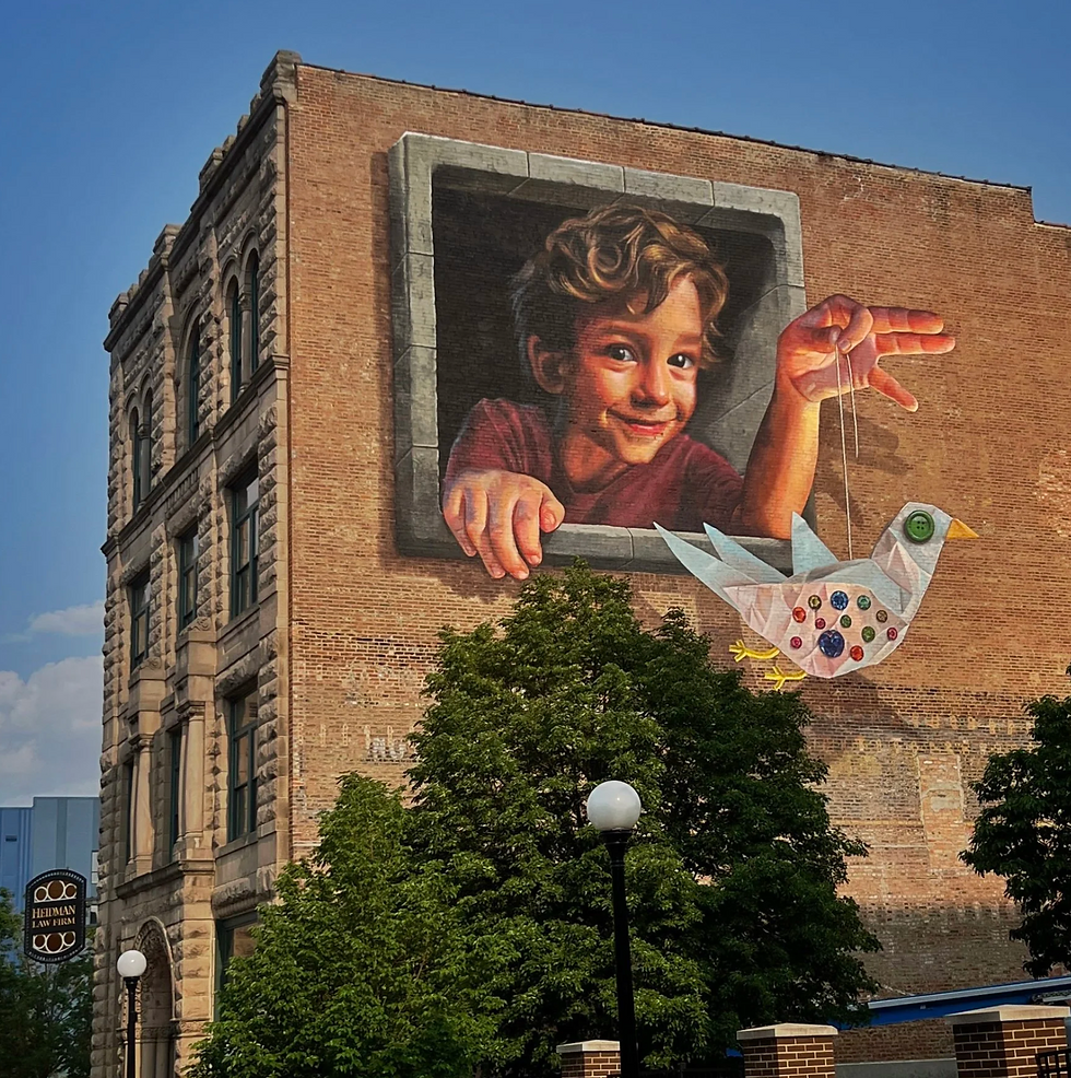 Naomi Haverland mural of a child leaning from a trompe-l'oeil window while controlling a handmade bird marionette on a brick building.