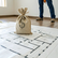 A money bag on floor plans, dollar symbol visible. Person in jeans stands nearby on wooden floor, suggesting construction or investment.
