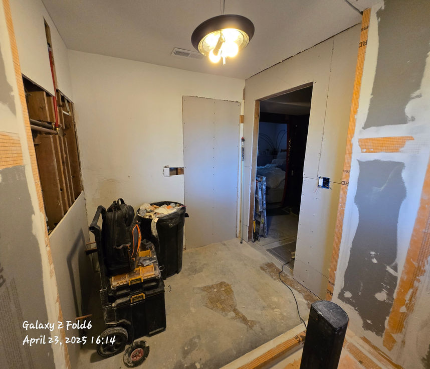 Partially finished bathroom showing waterproofed shower walls on the right, a newly drywalled section where an old doorway was in-filled, and a new open doorway leading into another room on the left.