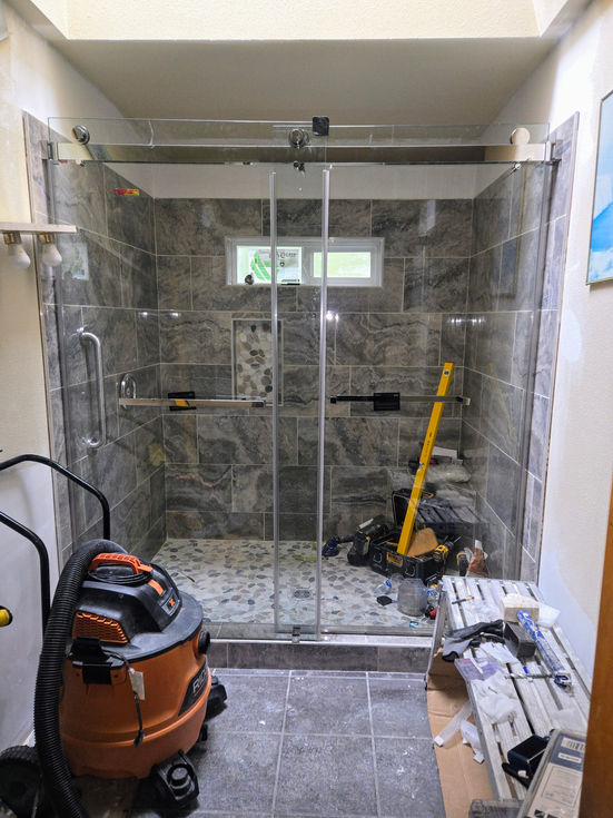 Front view of the tiled walk-in shower, now enclosed by a newly installed sliding glass door system with chrome header bar and handle.