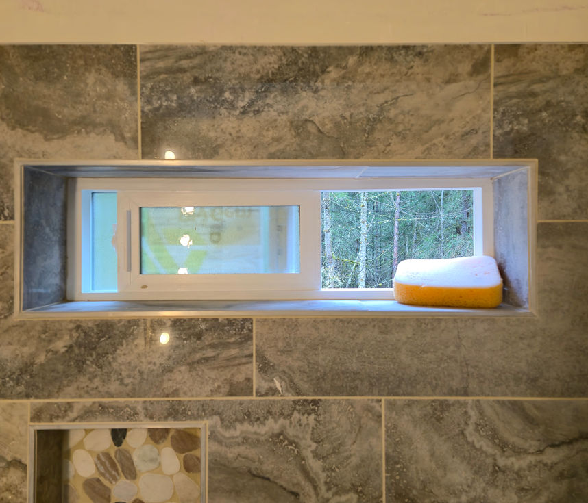 Close-up view of a horizontal window inside the shower, showing how the surrounding large grey wall tiles neatly wrap the window's interior frame and sill.