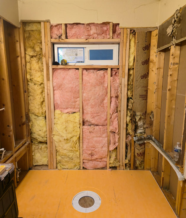 An orange, pre-fabricated Schluter shower tray with a central drain opening installed in the framed shower enclosure; walls show exposed studs and insulation.