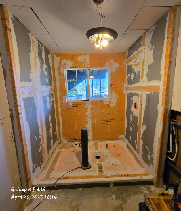 Master bathroom shower enclosure with grey DensShield boards on side walls and orange Schluter fabric on the back wall, all seams taped for waterproofing, awaiting tile.