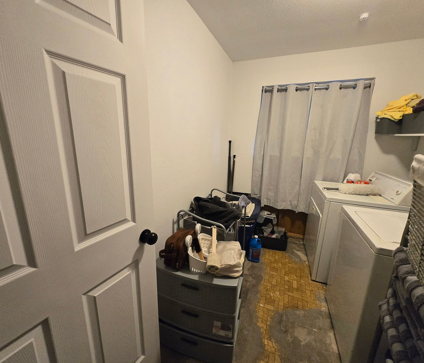 Angled view of an existing laundry room, showing the window and wall where the new master walk-in tiled shower will be built.