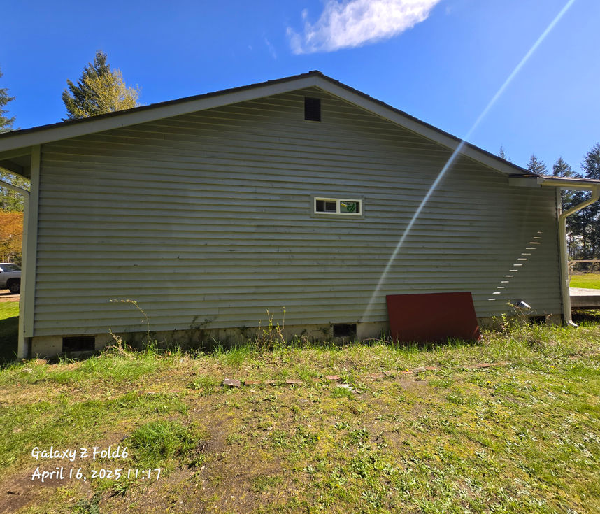 Exterior side view of a house with greenish-grey siding, showing a small horizontal window. The siding looks uniform, with no visible indication of the previous major wall repair.