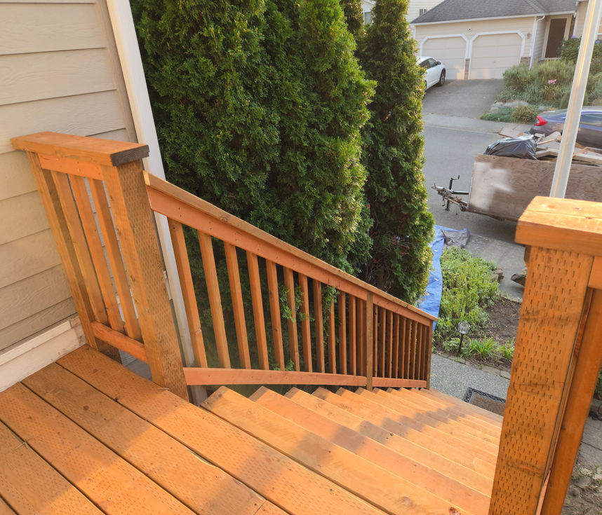 A high-angle view looking down the new deck stairs, showing the wooden railing and spindles.