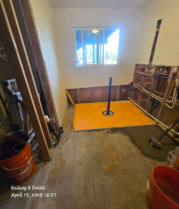 Newly poured concrete floor with an orange Schluter pre-sloped shower pan and black drain pipe installed in the center of the new bathroom.