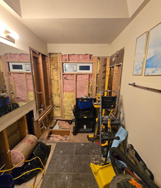 Interior view of bathroom under construction showing new timber framing and insulation installed on the back wall, featuring a new, small, horizontally oriented window