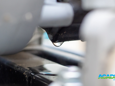 Close-up of a water droplet hanging from a black surface, set against a blurred gray and white background. "ACADEMY PUMP & MOTOR" text in blue.