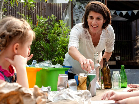 An educator guiding young students through a place-based sustainability and waste management lesson with recycling containers in a school garden.