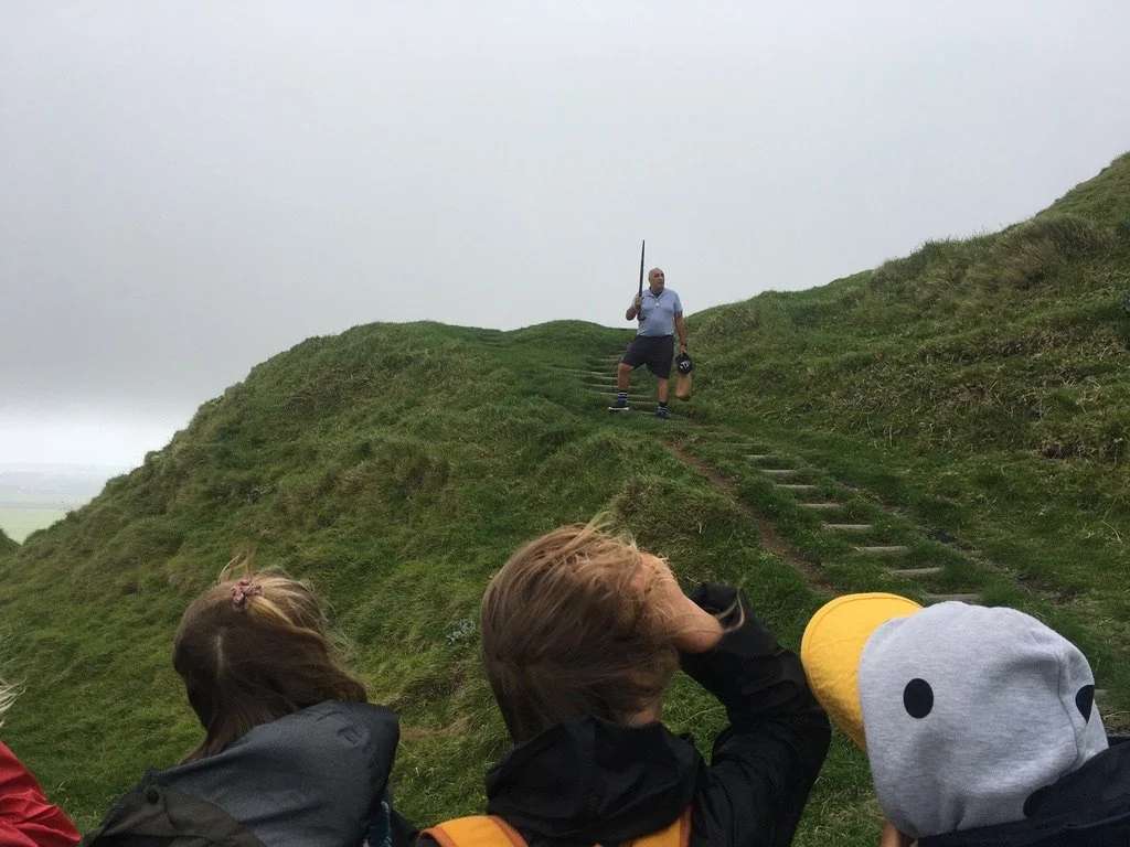 Educator leads a kōrero with students on a hillside, using the landscape to explore mātauranga Māori, navigation, and environmental knowledge.