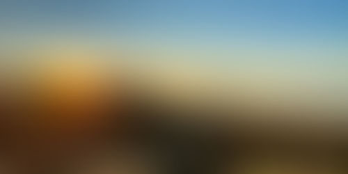 Golden sunrise over a quiet beach with dunes, calm sea, and a distant island under a clear blue sky.