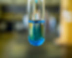A test tube with swirling blue liquid is suspended in a blurred laboratory setting, suggesting a scientific experiment.