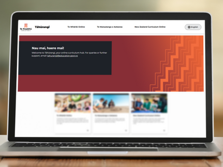 Laptop on a table shows the Tāhūrangi website with Māori text, a red-orange banner, and blurred curriculum cards below.
