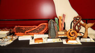 Table of carved wooden and stone trophies with plaques on a black cloth, against a red wall; one plaque reads Scion.