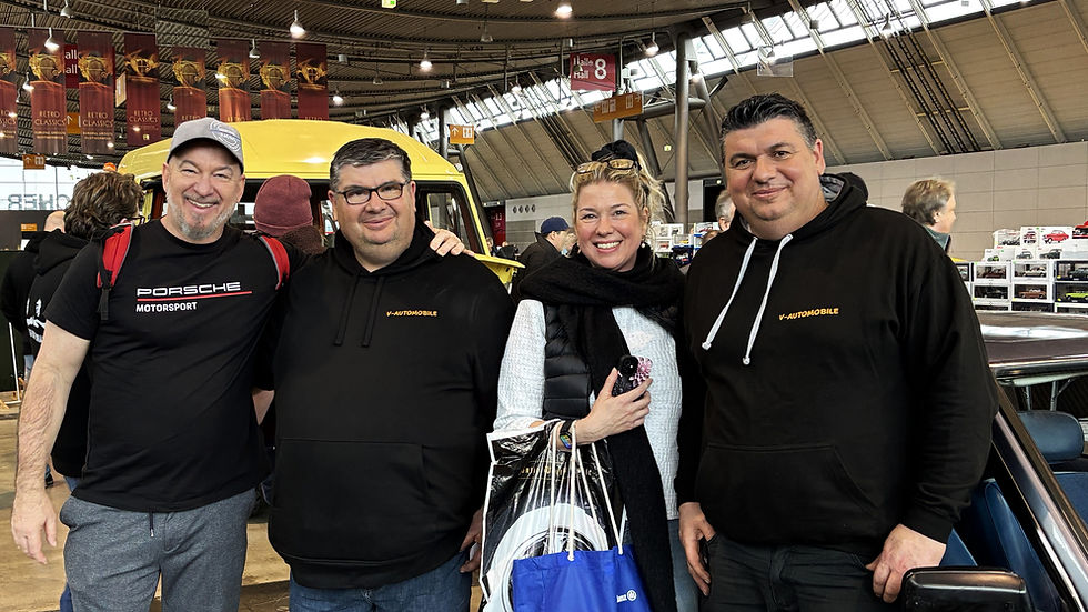 Vier lächelnde Besucher vor gelbem Oldtimer in Messehalle; Shirts mit Porsche Motorsport und V-Automobile, Retro Classics.
