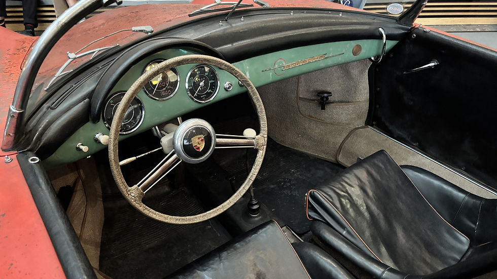 Innenraum eines alten Porsche-Roadsters mit abgewetztem Lenkrad, schwarzen Sitzen und grünem Armaturenbrett im Museum.