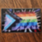 4 inch sticker of "Y'all Means All" a photo of a quilted progress pride flag held by hands with pride flags painted on them