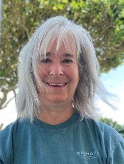 Woman with silver hair smiling outdoors, embracing herself fully